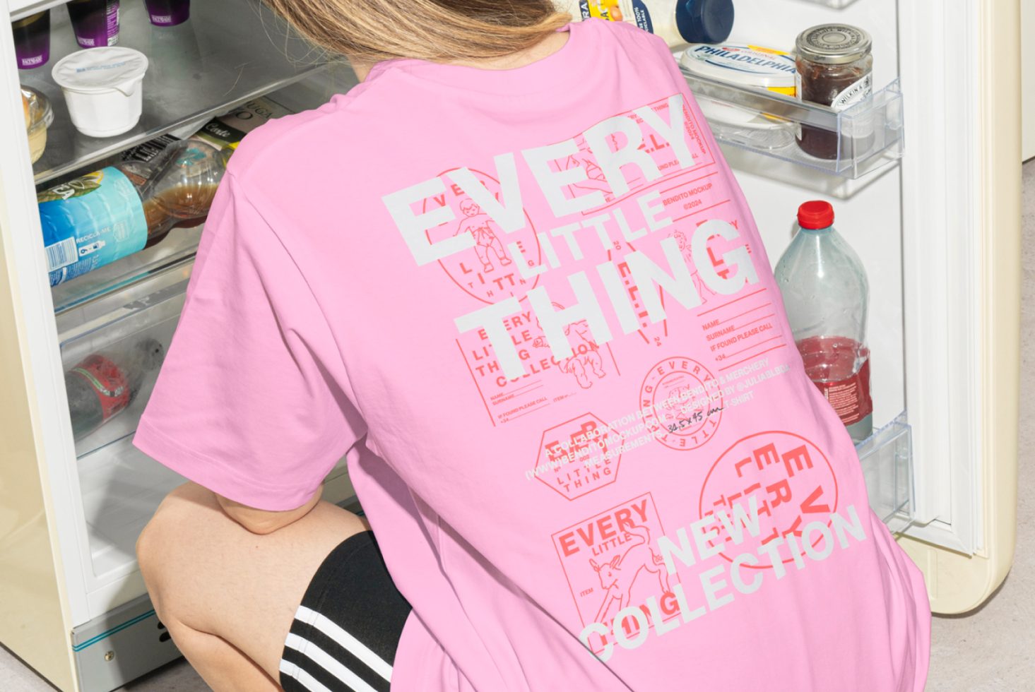 Person wearing a pink graphic t-shirt kneels in front of an open refrigerator. T-shirt has bold text overlay design. Mockup, template for designers.