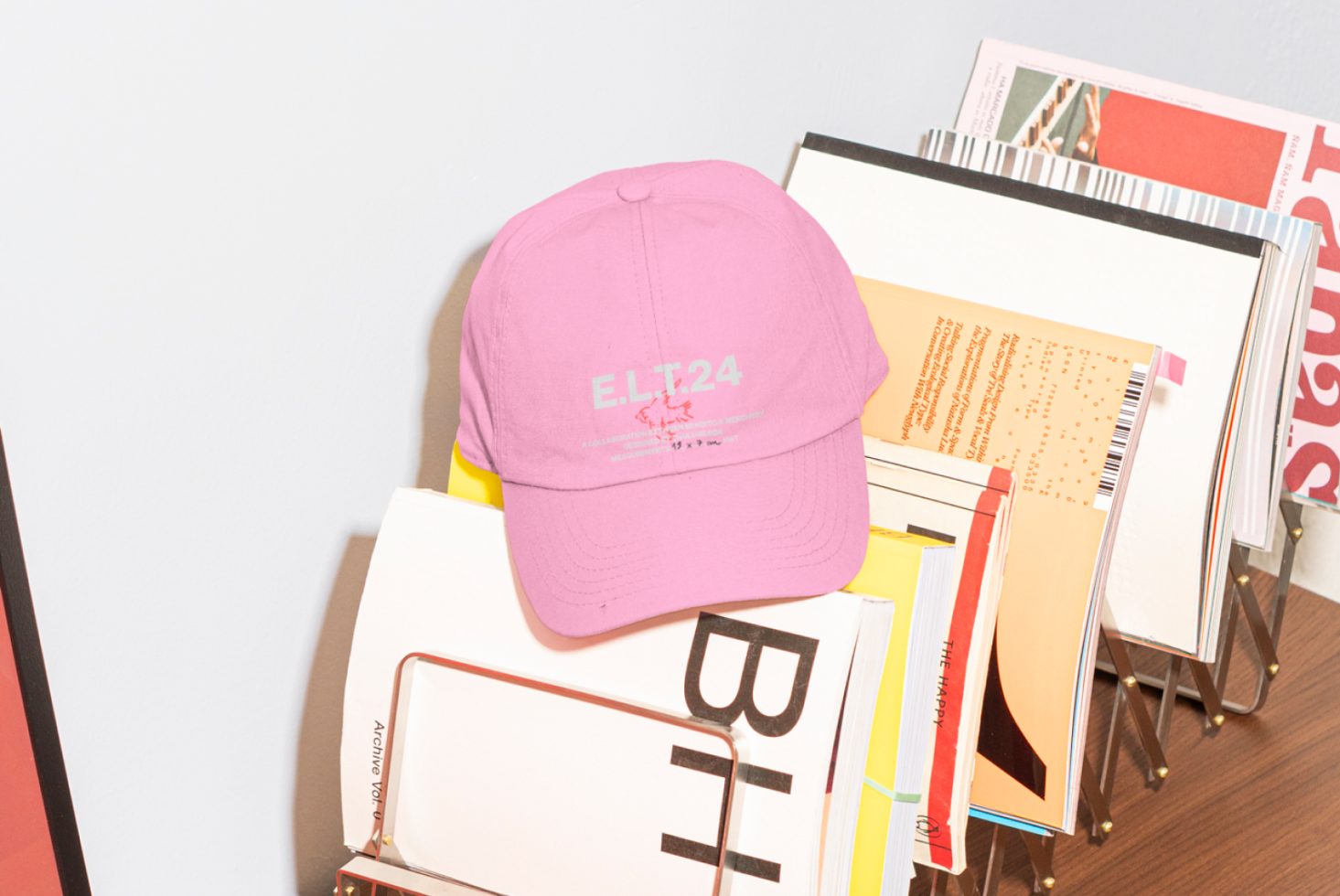 Pink baseball cap with text ELT24 sitting on colorful books and magazines. Perfect for use in mockups, templates, graphics, and designer projects.