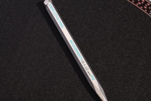 Silver metal pen on a black surface with teal text reading Every Little Thing Measurements on the pen body. Ideal for designers seeking mockups and graphics.