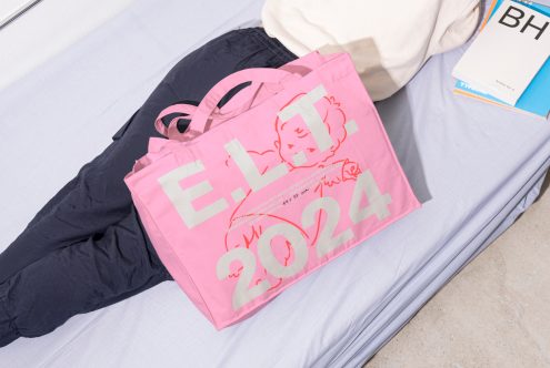 Mockup of a pink bag with bold white text E.L.T. 2024, perfect for designers. Displayed on a bed, it also features an abstract graphic design.