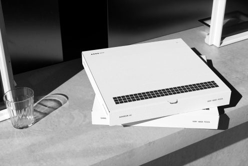 Monochrome mockup of two pizza boxes on a concrete surface next to a glass of water. Keywords: Mockup Pizza Box Minimalist Design Packaging.