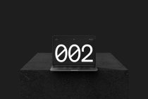 Laptop on concrete table displaying bold 002 typography in center