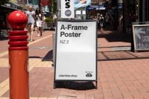 A-frame street poster mockup on busy urban sidewalk with red bollard