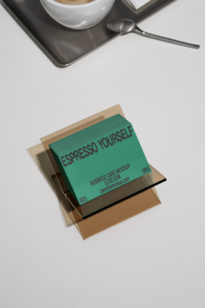 Business card mockup featuring green cards with playful text displayed on a layered glass stand blurred background includes coffee cup and spoon design tool.