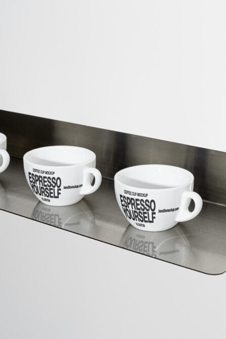 Two white espresso cups side by side on dark steel shelf