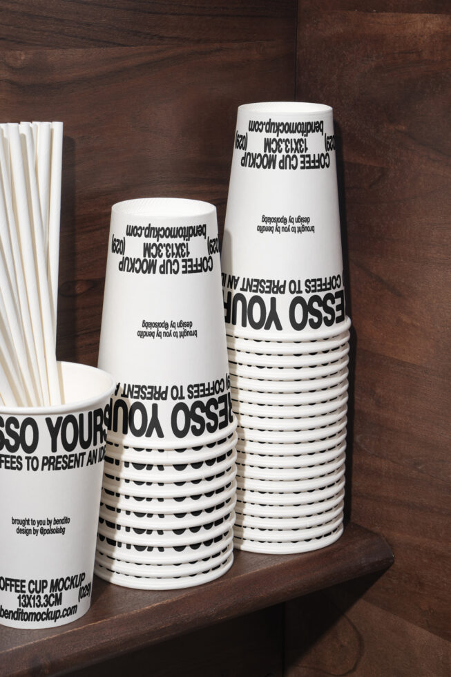 Stack of white paper coffee cups with bold black text design mockup on a wooden shelf ideal for branding and packaging template for designers.