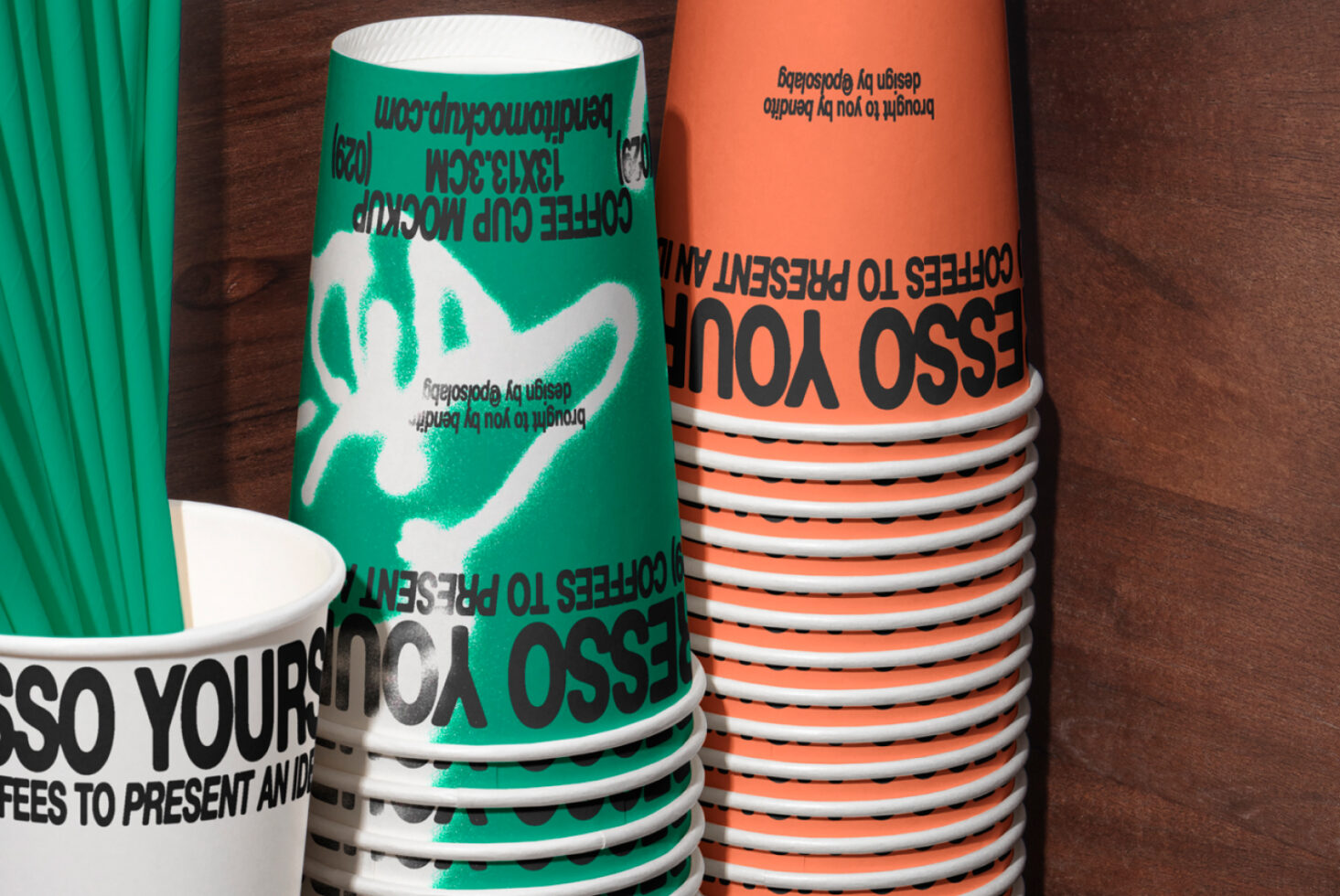 Stacked disposable coffee cups with bold text designs in green and orange for a mockup template to enhance branding and packaging design.