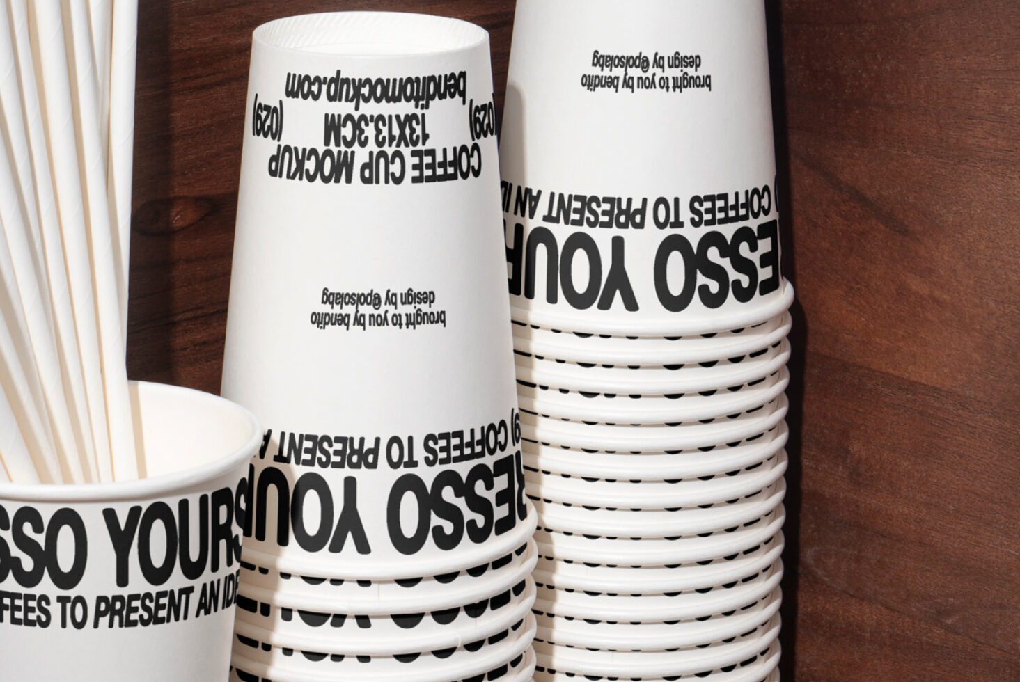 Stack of paper coffee cups with bold black text design mockup on wooden surface. Ideal for graphic designers seeking creative branding templates.