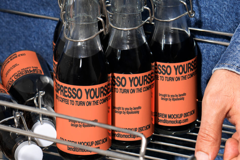 Close-up of coffee bottle mockups with orange labels in a metal basket. Hand reaching for a bottle. Ideal for graphic design and packaging projects.