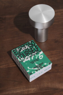 Magazine stack with green espresso cover next to brushed metal cylinder on wood