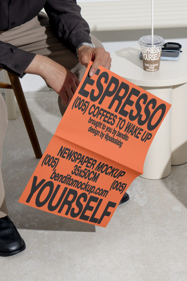 Man holds bold orange newspaper mockup with black text beside a table with coffee cup also labeled mockup. Ideal for designers seeking modern templates.