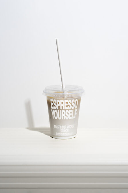 Plastic cup mockup featuring a lid and straw on a white surface; ideal for showcasing branding designs in product templates; suitable for designers.