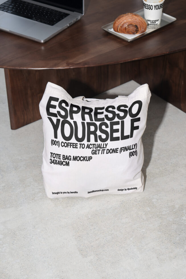 Tote bag mockup on concrete floor with laptop and coffee on wooden table. Bold text display. Ideal for branding, design presentations, templates, graphics.