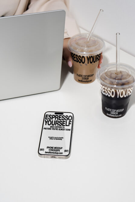 Workspace setup featuring iPhone mockup, laptop edge, two iced coffee cups on white
