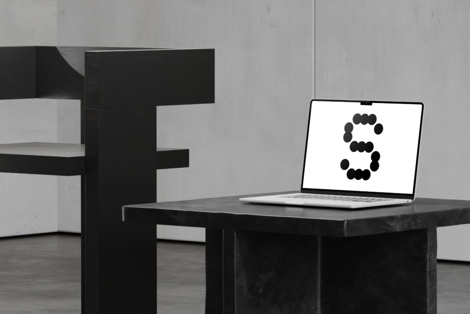 Laptop on dark desk with geometric sculpture behind it