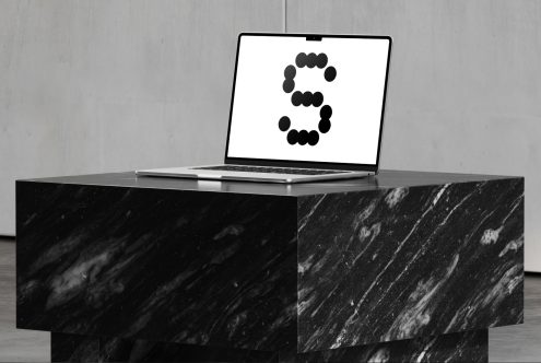 Open laptop displaying a stylized letter S in black dots, set on a black marble podium. Suitable for mockups, graphic design resources, templates.