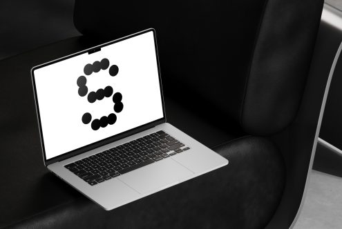 Laptop with a modern design font mockup on screen resting on a black leather couch. Ideal for showcasing typography in digital graphic design projects.