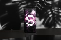 Smartphone with white circles on purple liquid swirl, blurred plant backdrop