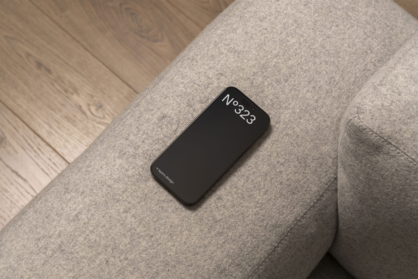 Smartphone mockup resting on a modern gray couch with wooden floor background. Ideal for UX UI design presentations and digital product showcases.