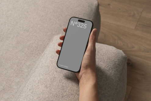 Hand holding smartphone with blank screen for mockup design. Cozy interior setting with soft texture. Ideal for designers and digital assets. Templates.