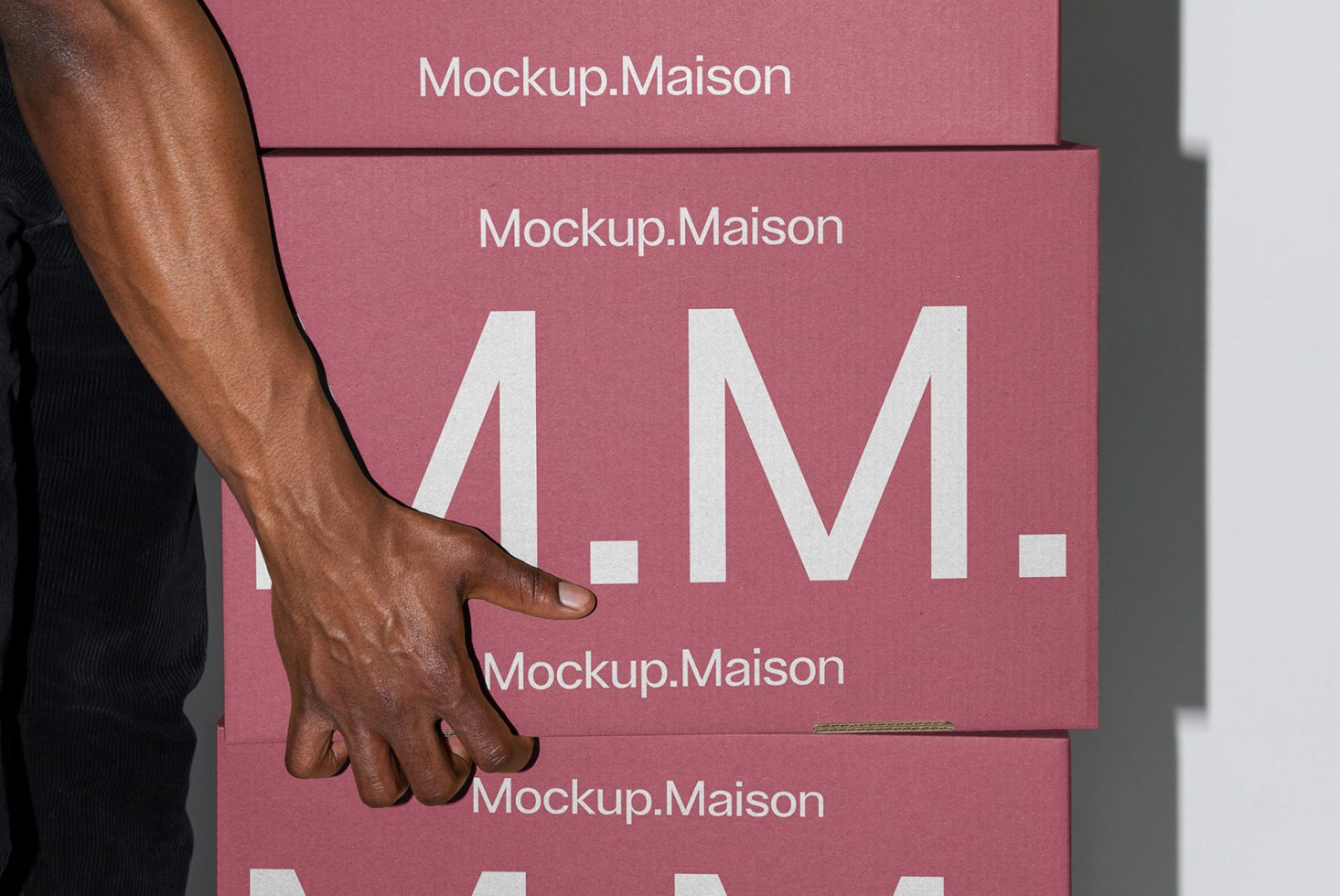 Stacked red boxes labeled Mockup Maison, with a person's hand holding one box. Suitable for packaging mockups. Ideal for designers and digital assets.