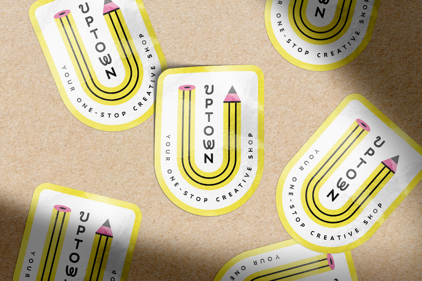Custom sticker mockup on textured paper background featuring a yellow pencil design and typography reading Uptown Your One-Stop Creative Shop. Perfect for branding.