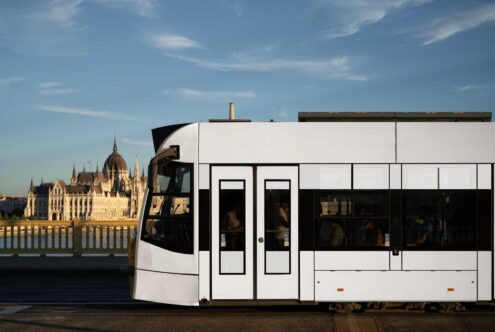 Modern city tram passing along a bridge with a historic building backdrop under a blue sky perfect for urban-themed graphic design and template use