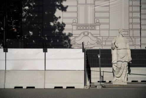 Statue behind construction fence with urban backdrop suitable for mockups or templates in architectural design projects. Shadow play enhances depth.