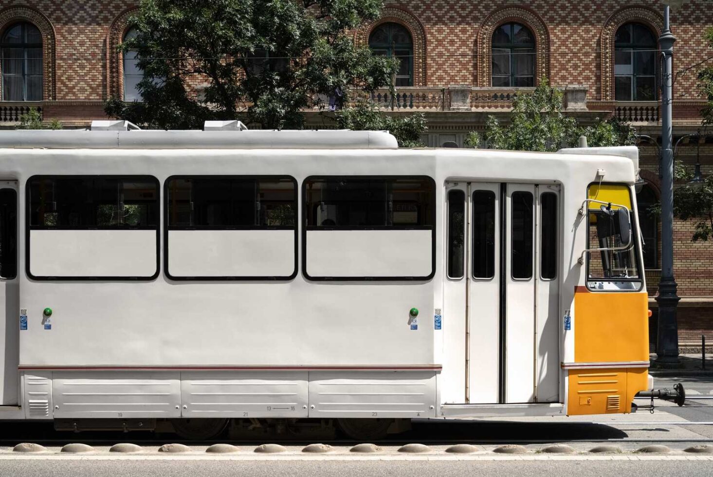 Side view of a modern tram with a yellow front on a city street showing architectural brick building in the background urban transportation mockup