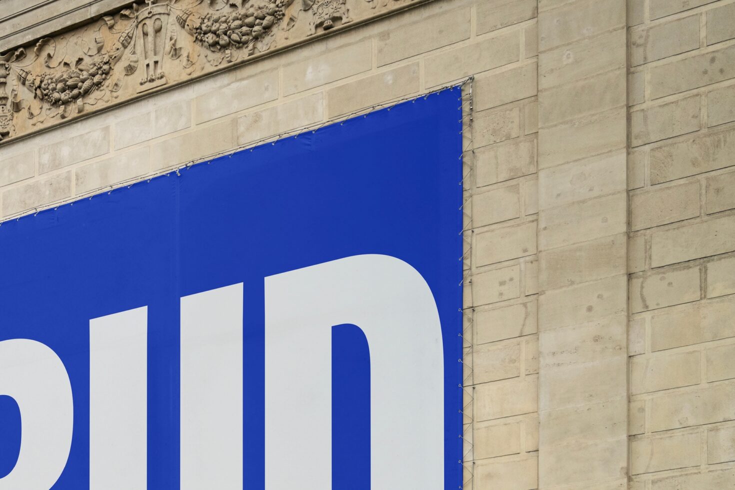 Close-up of a large blue banner with bold white typography against a textured stone wall background, ideal for graphic designers and typographic templates.