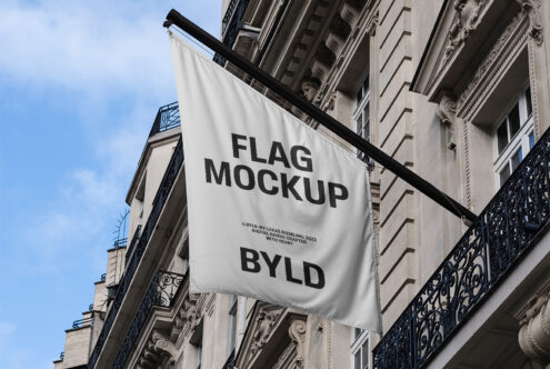 Urban flag mockup hanging on classic building facade against blue sky suitable for designers showcasing branding or advertising concepts.