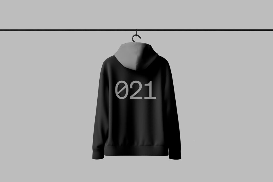 Black hoodie mockup with the number 021 on the back hanging on a rack against a gray background. Ideal for designers in need of apparel templates.