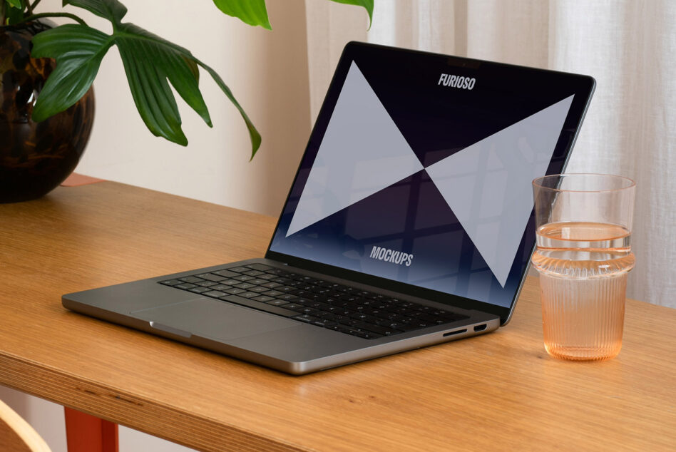 Laptop on wooden desk with blank screen mockup template for designers. Nearby is a glass of water and a plant. Perfect for design presentations.