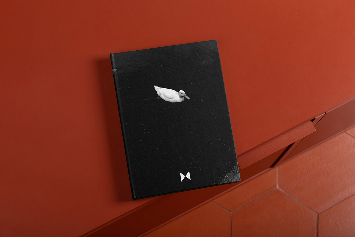 Mockup displaying a black notebook with a white duck design on an orange surface background. Ideal for showcasing cover designs and branding concepts.