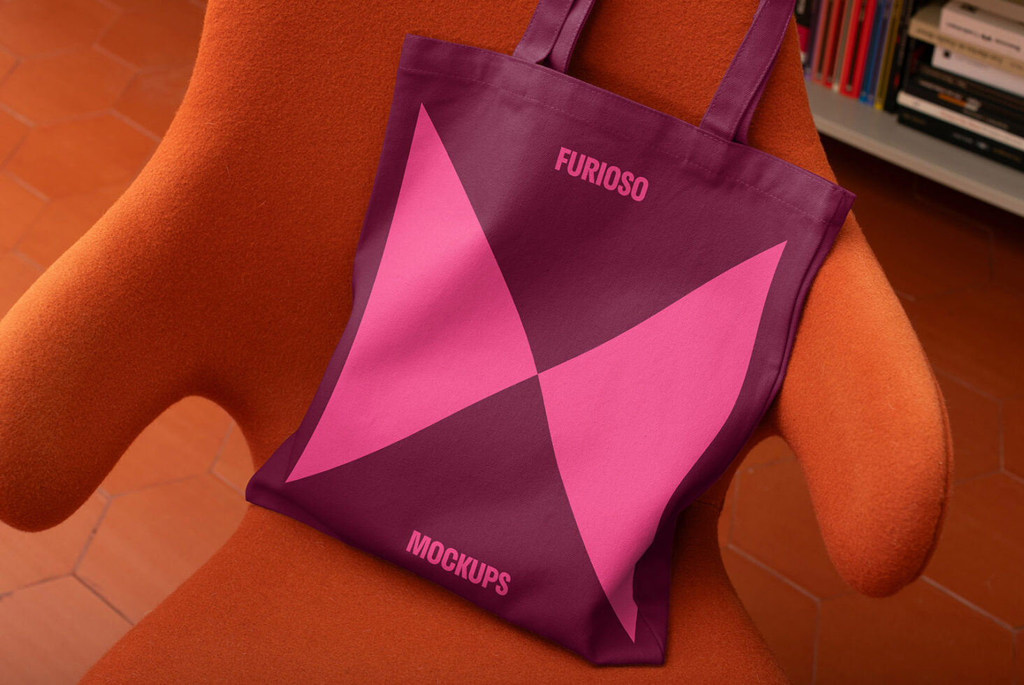 Tote bag mockup with bold geometric design in pink and burgundy on orange chair. Ideal for showcasing branding and design projects to graphic designers.