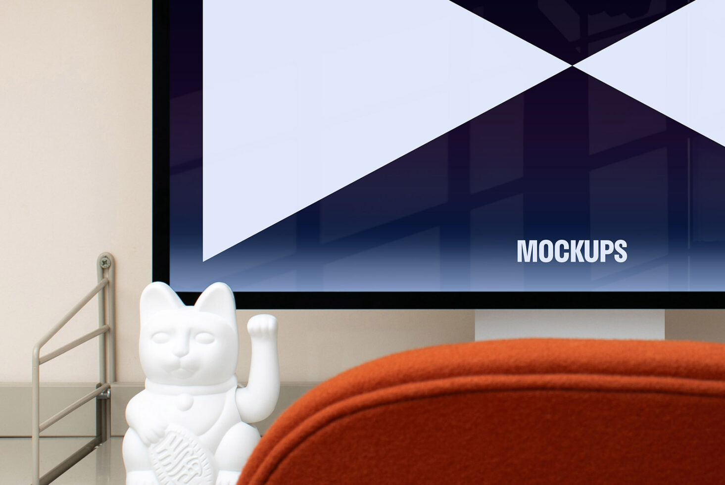 Modern workspace mockup featuring a computer monitor displaying the word mockups, with a minimalist cat sculpture and an orange chair in the foreground.