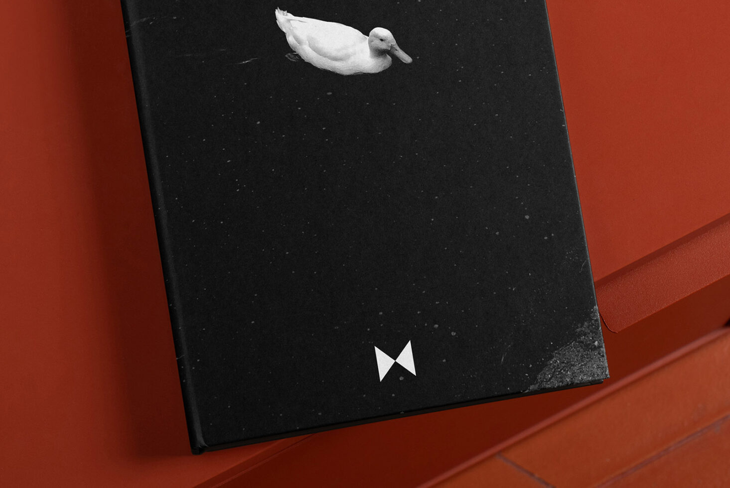 Black hardcover book with a white duck illustration and geometric logo on an orange surface. Ideal for designers seeking unique graphics and modern book covers.