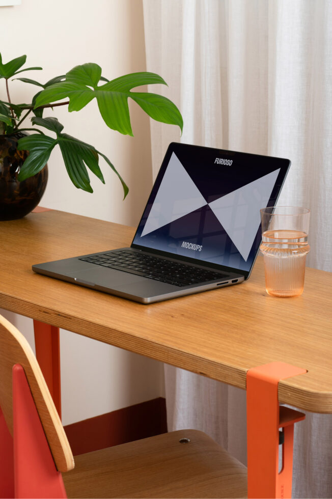 Laptop mockup on a wooden desk with a plant and a glass. Perfect for showcasing digital assets for designers. Keywords: mockups designers workspace.