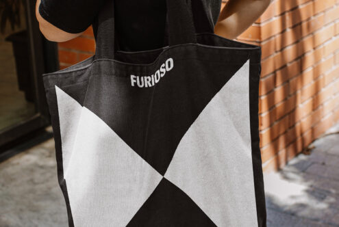 Black and white geometric tote bag with text Furioso carried by person; suitable for branding mockups or graphic design assets for designers.