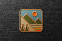 Retro badge icon with mountains, trees, sun in gold embossed style on dark fabric