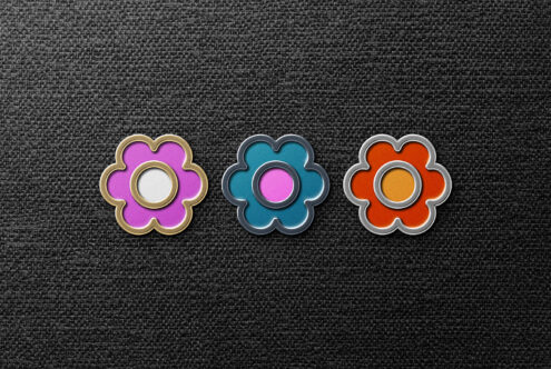 Three colorful flower-shaped enamel pins in pink, blue, and orange on black textured background. Perfect for designers seeking unique graphics or mockups.