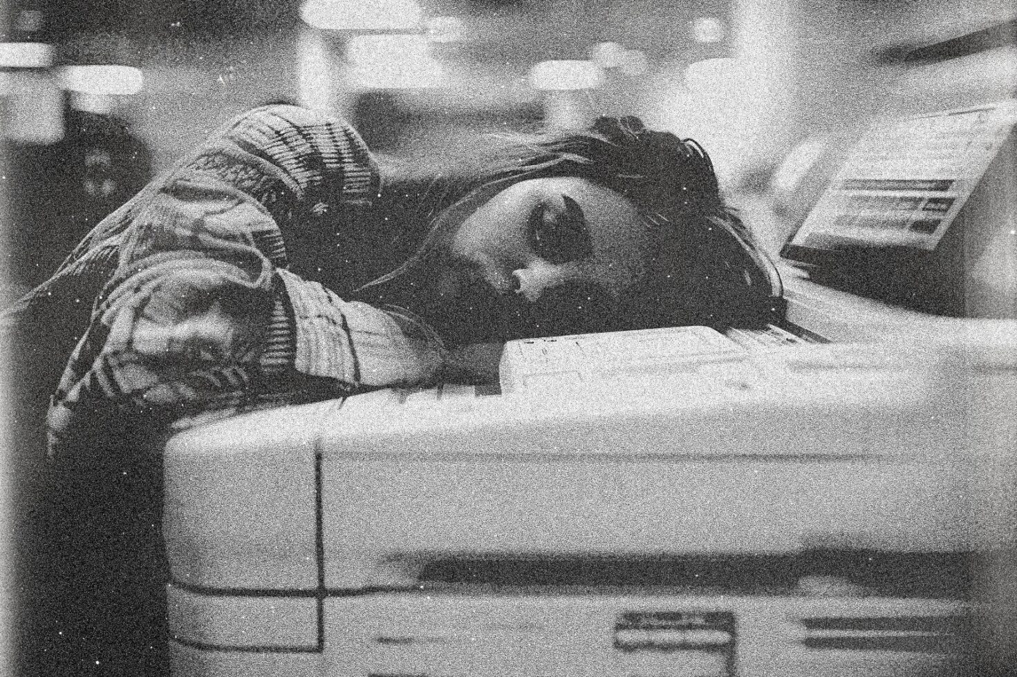 Grainy black and white image of a woman in a plaid shirt resting her head on a photocopier. Perfect for designers seeking vintage photography effects.