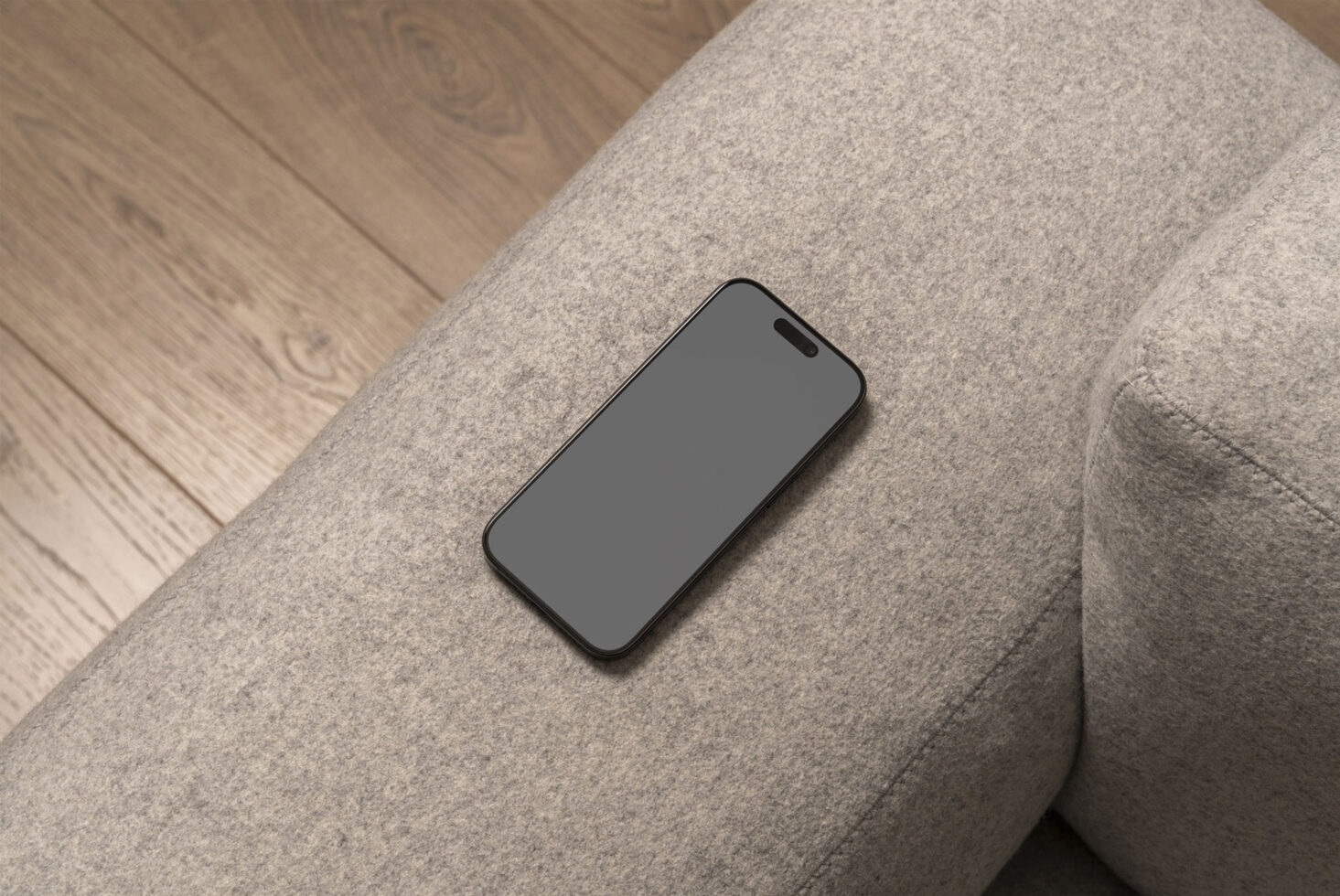 Smartphone mockup on a grey fabric sofa with wooden floor background suitable for digital asset marketplaces for designers searching for mockups.