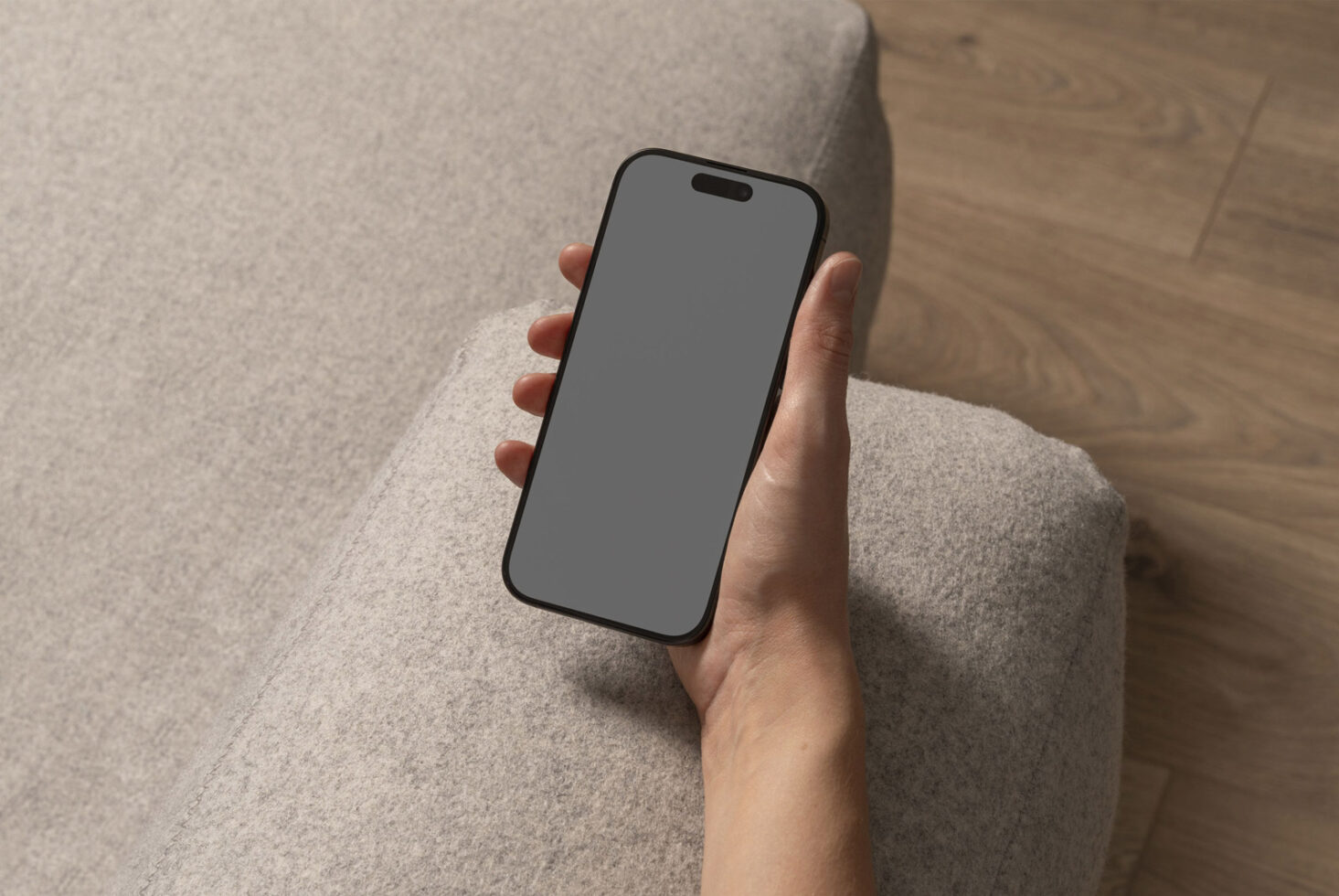 Mockup of a hand holding a smartphone with a blank screen on a gray fabric surface. Perfect for showcasing mobile app designs or responsive web layouts.