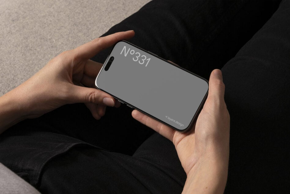 Hands holding iPhone 16 Pro in landscape with gray screen on dark clothing