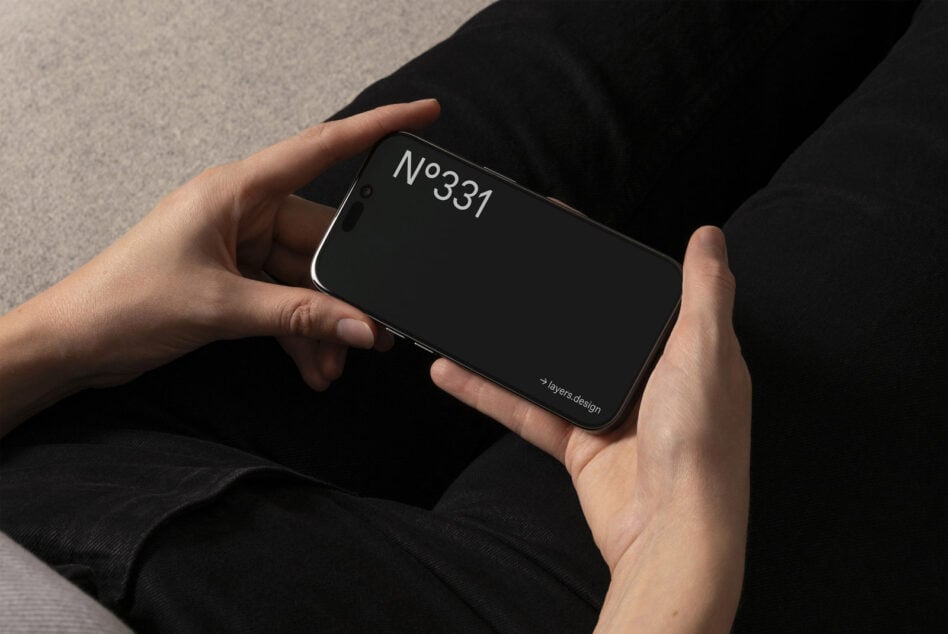 Hands holding iPhone 16 Pro horizontally with dark display in lap shot