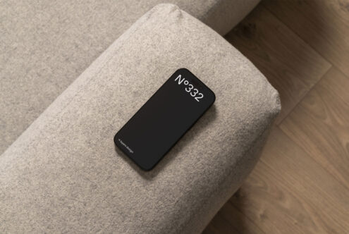 Smartphone mockup on a grey upholstered couch, showcasing minimal design for mobile interfaces and app presentations, ideal for designers and UX/UI projects.