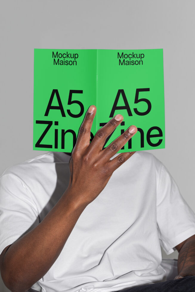 Mockup image of person holding open A5 zine in vibrant green cover displaying bold typography. Ideal for designers seeking zine and layout mockups.