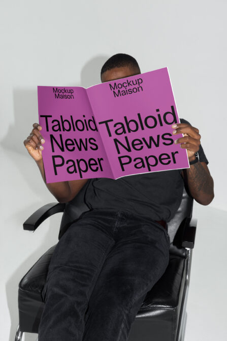 Person sitting in chair holding open magenta magazine mockup with Tabloid News Paper text