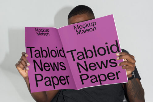 Designer holding a customizable tabloid newspaper mockup with a purple cover ideal for showcasing graphic designs and templates for creative projects.